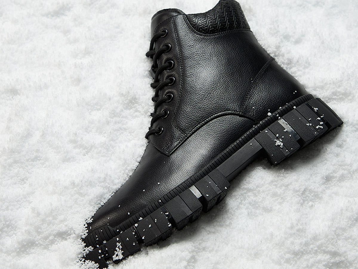 Black leather boot with a thick sole on a snowy background.