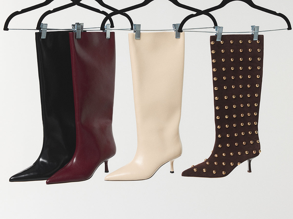 Collection of women's high-heeled boots in various colors and styles on hangers on a light background